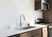 Thumbnail 8 of 9 - A modern kitchen with a stainless steel sink and a microwave above the stove.