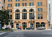 Thumbnail 1 of 9 - A large, old building with many windows sits on a city street corner.