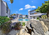 Thumbnail 9 of 23 - A pool surrounded by rocks and plants with a building in the background.