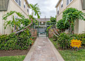 Thumbnail 2 of 15 - a walkway between two apartment buildings with a fence and palm trees
