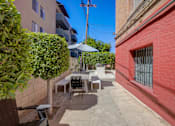 Thumbnail 37 of 40 - A patio with a table and chairs is surrounded by a brick wall and a green bush.