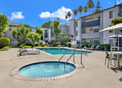 Thumbnail 7 of 23 - A swimming pool surrounded by a patio with chairs and umbrellas.