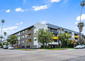 Thumbnail 1 of 19 - A modern apartment building with a parking lot in front.