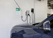 Thumbnail 16 of 23 - A blue car is plugged into an electric vehicle charging station.