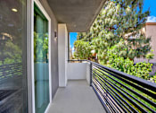 Thumbnail 11 of 23 - A balcony with a black railing and a glass door leading to a lush green outdoor area.