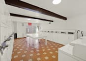 Thumbnail 18 of 23 - A laundry room with a washer and dryer on the right and a white table in the middle.