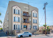 Thumbnail 1 of 12 - A white car is parked in front of a two-story building with a balcony.