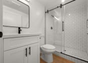 Thumbnail 9 of 14 - A white toilet sits in a bathroom with a walk-in shower.