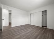 Thumbnail 46 of 64 - A room with white walls and wood flooring with a door on the left and a closet on the right at Sunset Square, West Covina, 91790