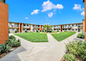 Thumbnail 5 of 64 - an exterior view of a courtyard at an apartment building with green grass at Sunset Square Apartments, West Covina, California, 91790
