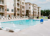 Thumbnail 6 of 21 - A swimming pool surrounded by lounge chairs in front of apartment buildings.