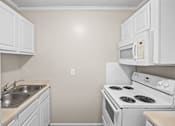 Thumbnail 12 of 20 - A white kitchen with a stove, sink, and microwave.