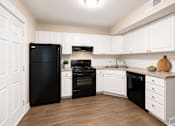 Thumbnail 5 of 21 - A black refrigerator is in a kitchen with white cabinets.