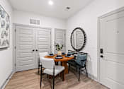 Thumbnail 13 of 19 - A dining room with a round mirror and a table with chairs.