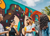 Thumbnail 19 of 21 - Four women are standing in front of a colorful mural.