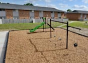 Thumbnail 5 of 13 - A playground with a green slide and swings in front of a brick building.