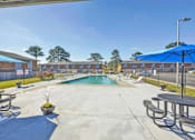 Thumbnail 12 of 13 - A pool area with a blue umbrella and picnic tables.