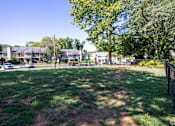 Thumbnail 4 of 11 - A grassy area with a dirt path and a fence in the foreground with houses in the background.