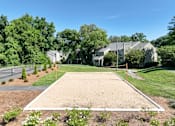 Thumbnail 2 of 11 - A sand volleyball court is surrounded by trees and houses.