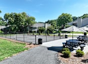 Thumbnail 3 of 11 - A sunny day at a park with picnic tables and a tennis court.