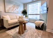Thumbnail 10 of 12 - A living room with a white couch, a wooden coffee table, and a large window.