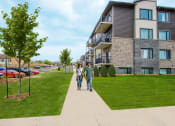 Thumbnail 3 of 11 - two people walking down a sidewalk in front of an apartment building