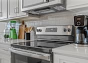 Thumbnail 6 of 19 - A modern kitchen with a stove top and a coffee maker.