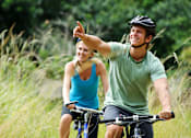 Thumbnail 12 of 19 - A man and a woman are riding bicycles in a grassy area.