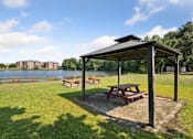 Thumbnail 6 of 14 - Picnic table and pavillion in a park with a lake in the background.