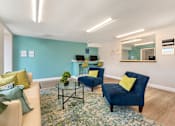 Thumbnail 19 of 22 - A living room with a blue chair and a glass table.