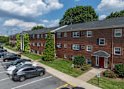 Thumbnail 24 of 51 - A parking lot with cars parked in front of a brick building.