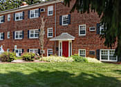 Thumbnail 16 of 51 - A red brick building with a red door and green bushes in front.