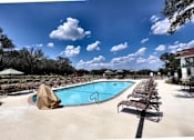 Thumbnail 14 of 56 - A large outdoor swimming pool with sun loungers and a tree in the background.