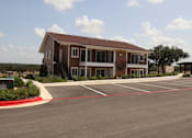 Thumbnail 7 of 56 - A brown building with a red roof and a parking lot in front.
