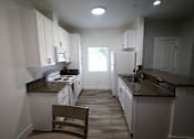 Thumbnail 27 of 56 - A kitchen with white cabinets and a brown chair.