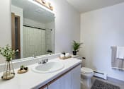 Thumbnail 11 of 14 - A white bathroom with a sink, mirror, toilet, and a plant.