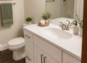 Thumbnail 5 of 11 - A white bathroom with a toilet, sink, and a green towel hanging on the towel rack.