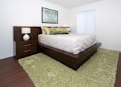 Thumbnail 6 of 17 - A bedroom with a bed, nightstand, and rug.