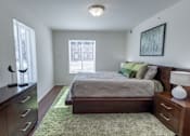 Thumbnail 8 of 14 - A bedroom with a bed, nightstand, and a window with blinds.
