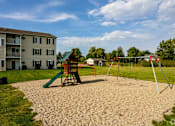 Thumbnail 4 of 14 - A playground with a green slide and a red swing set in front of a building.