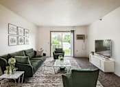 Thumbnail 7 of 14 - A living room with a green couch, a glass coffee table, and a flat screen TV.