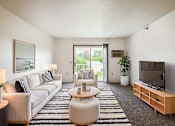 Thumbnail 2 of 14 - A living room with a white couch, a coffee table, and a television.