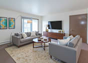 Thumbnail 1 of 15 - A living room with a grey couch, a coffee table, and a flat screen TV.