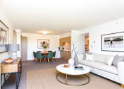 Thumbnail 2 of 15 - A living room with a white couch, a coffee table, and a dining table with chairs.