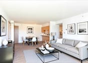 Thumbnail 9 of 14 - A modern living room with a grey couch, a glass coffee table, and a dining table with chairs.