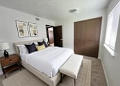 Thumbnail 10 of 13 - A bedroom with a large bed and a nightstand with a lamp.
