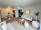 Thumbnail 3 of 13 - A living room with a white couch, a wooden coffee table, and a painting on the wall.
