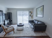 Thumbnail 2 of 14 - A living room with a black couch, a chair, and a television.