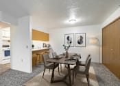 Thumbnail 2 of 11 - A dining room with a table set for two and a kitchen area in the background.