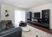 Thumbnail 2 of 17 - A black leather couch sits in a living room with a television and a fireplace.